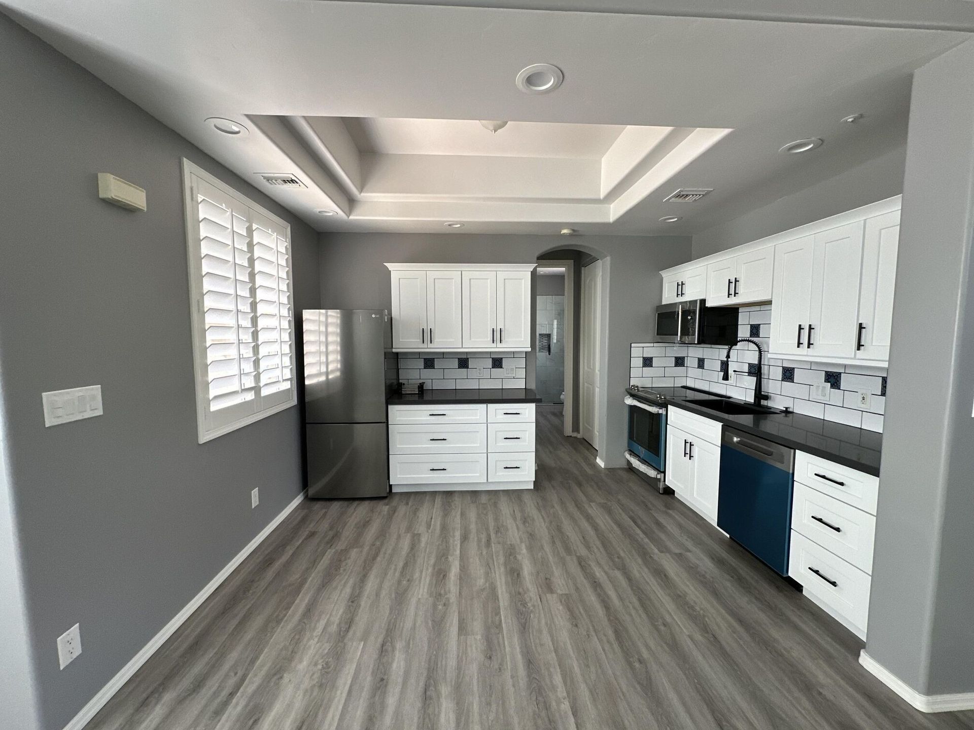 Gray-walled kitchen with white cabinets, stainless steel appliances, and wood-look flooring.