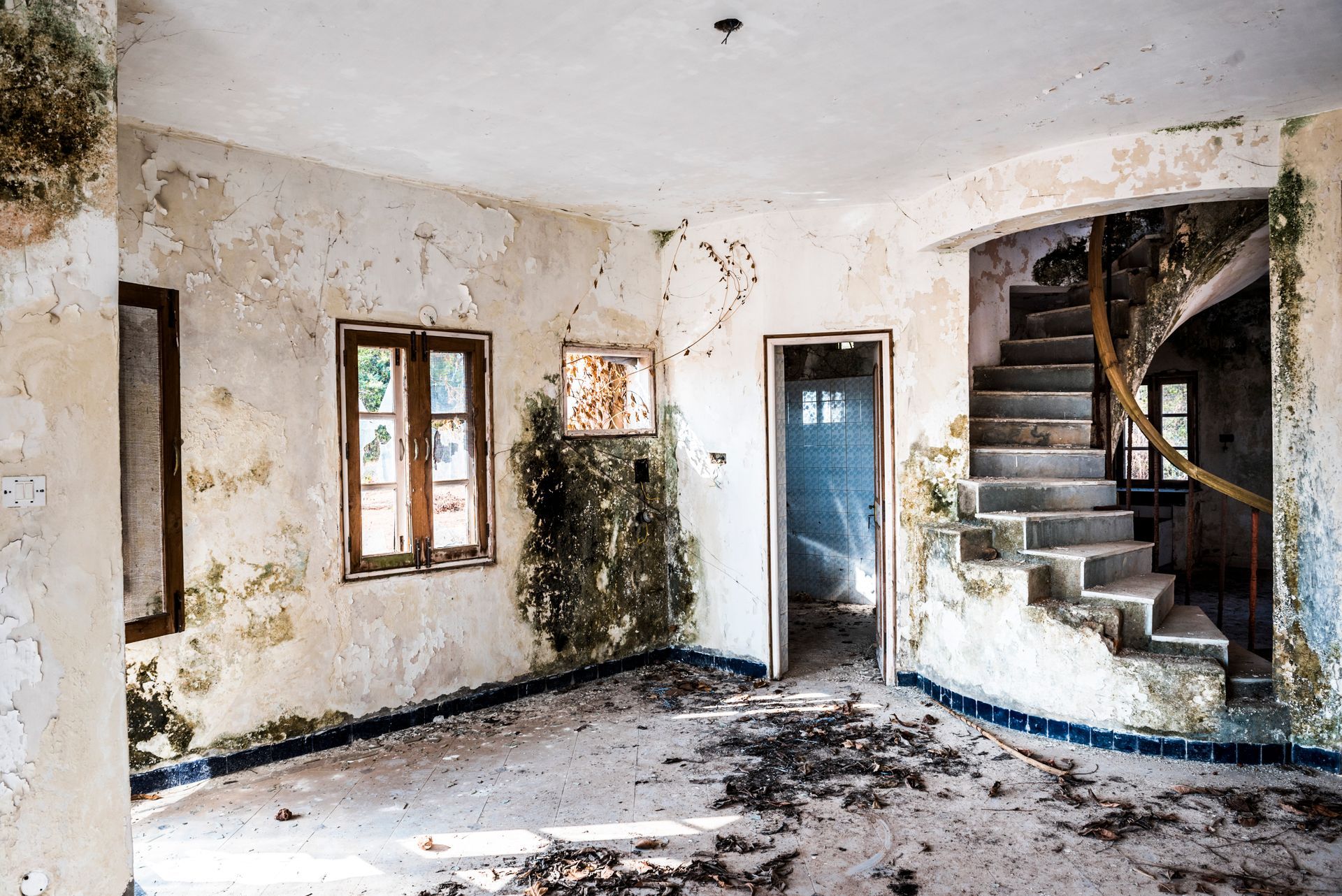 Interior of abandoned building, peeling walls with water damage, staircase, and broken window.