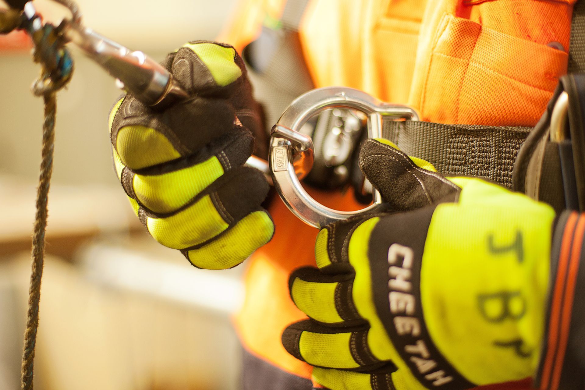 Close up of safety gloves securing a metal carabiner to a fall protection harness. Close up of safety gloves securing a metal carabiner to a fall protection harness.