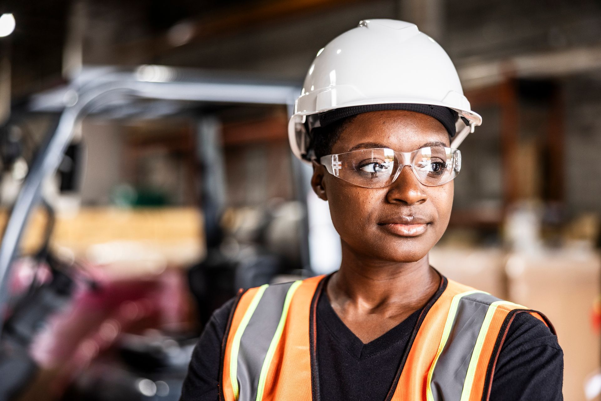 Construction worker wearing a white hard hat and safety vest in an industrial setting.