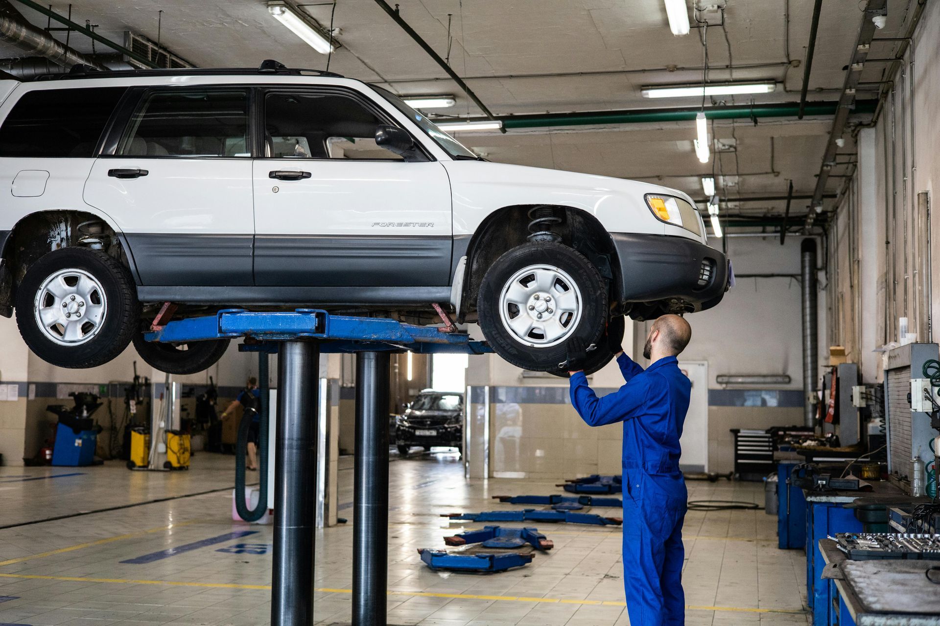 A man is working on a car on a lift in a garage.