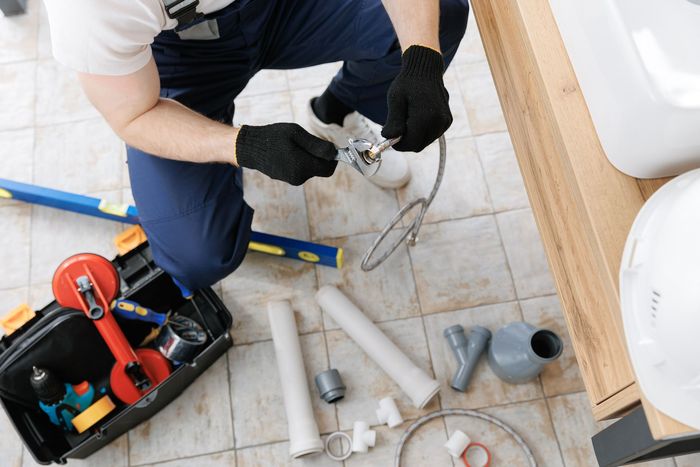 A plumber is working on a pipe in a bathroom.