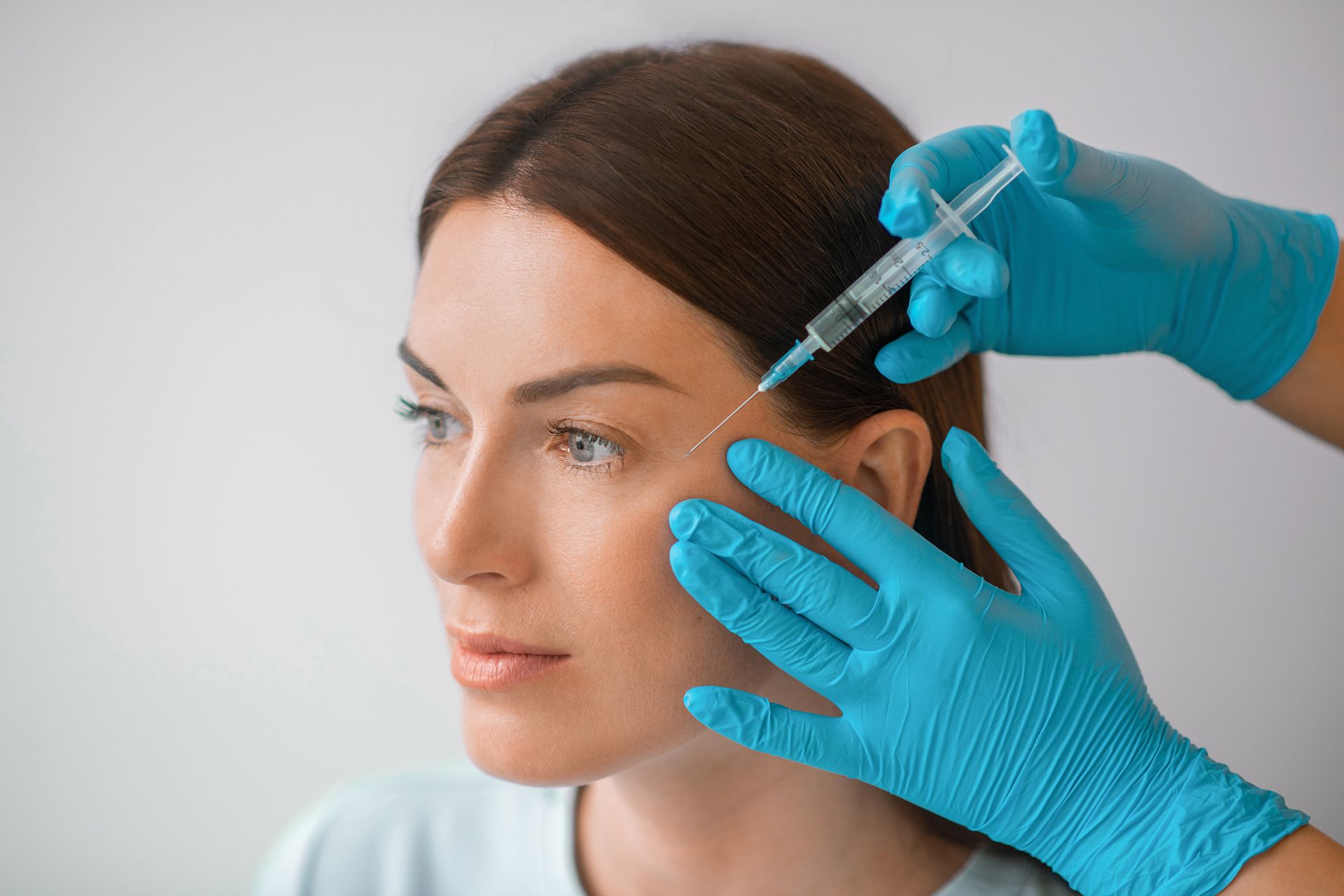 Woman receiving facial injection from gloved hands.