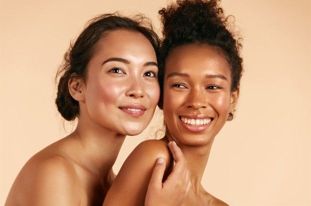 Two smiling people with glowing skin, embracing, against a cream backdrop.