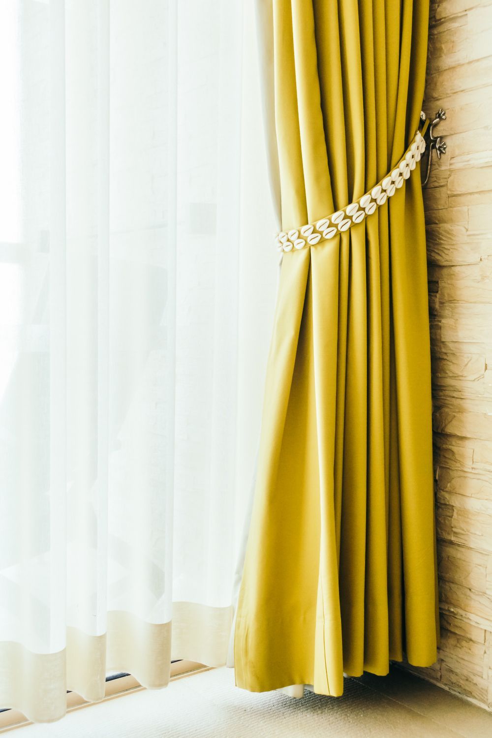 A yellow curtain is hanging on a window next to a white curtain.