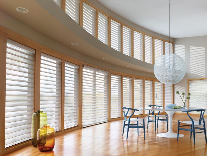 A dining room with a table and chairs and lots of windows with blinds