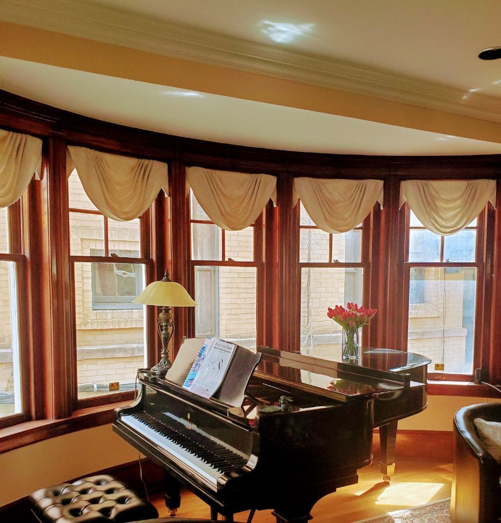 A piano in a living room with lots of windows with stylish Drapery