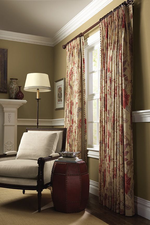 A living room with a chair, lamp and printed curtains installed on window