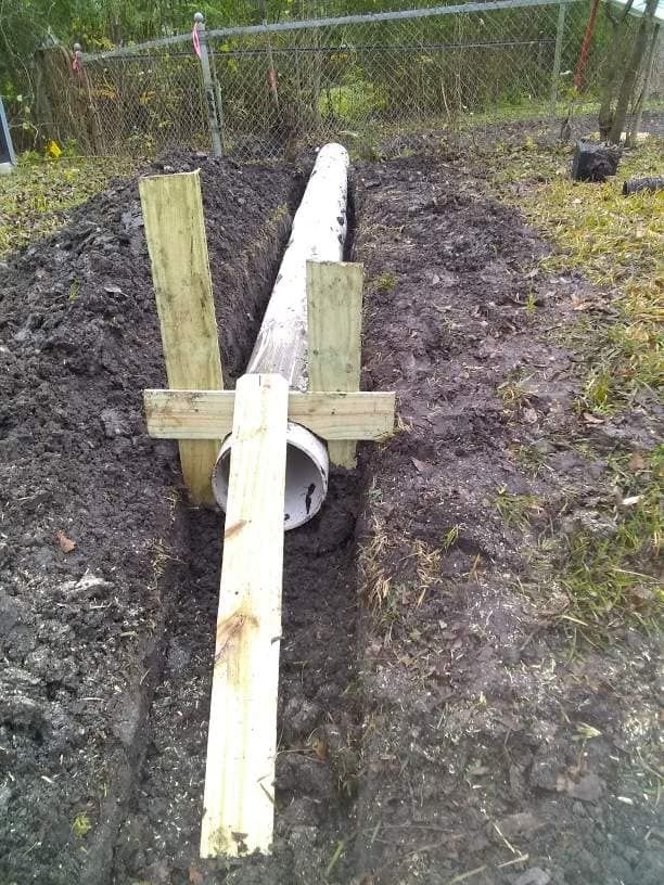 A pipe is sitting in the dirt next to a wooden post.