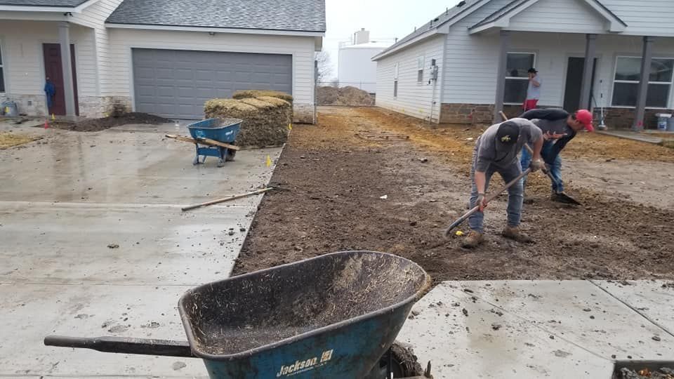 Two men are working on a driveway next to a wheelbarrow.