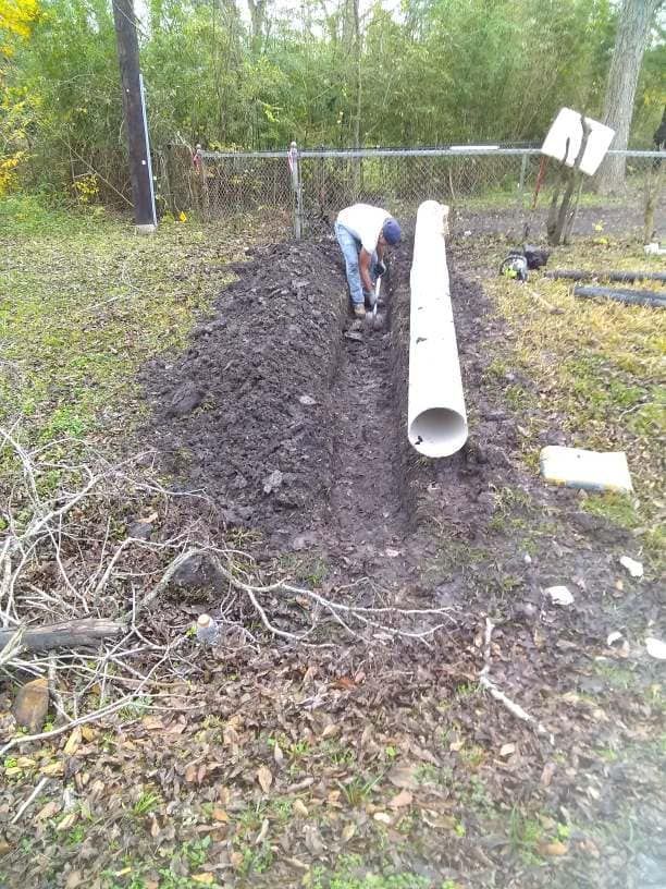 A man is working on a pipe in the dirt.