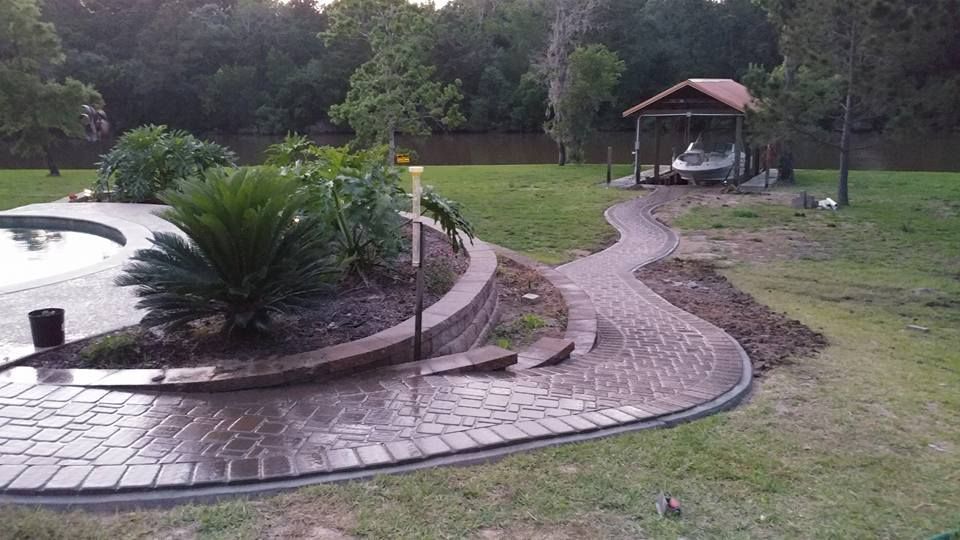 A brick walkway leading to a pool with a gazebo in the background