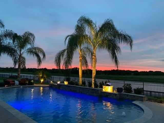 A swimming pool with palm trees and a sunset in the background