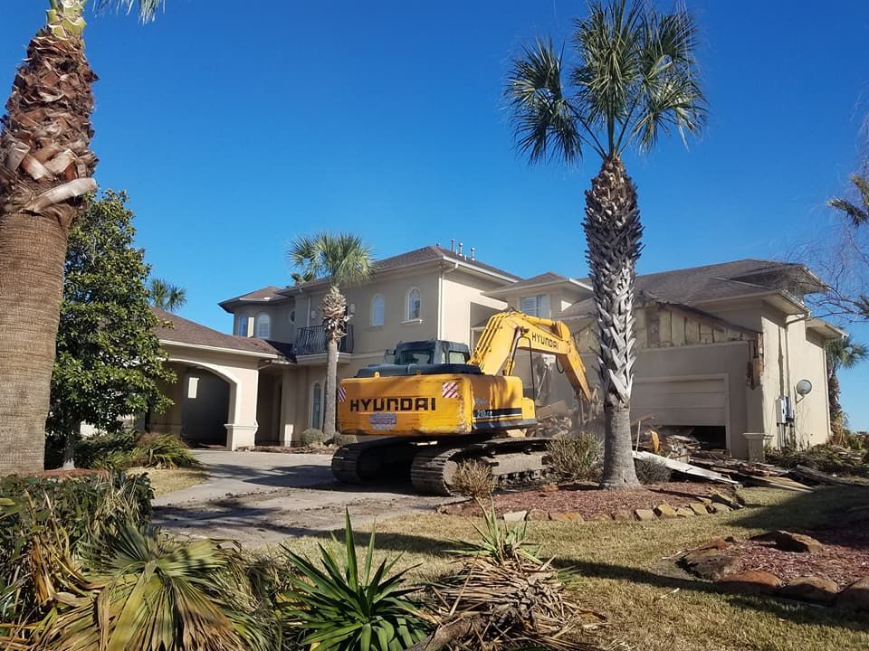 A large yellow excavator is parked in front of a large house.