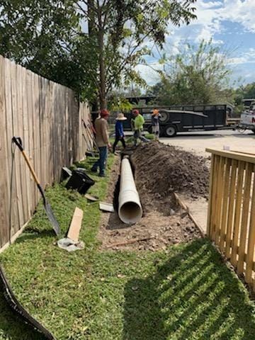 A group of men are working on a drain pipe in a yard.