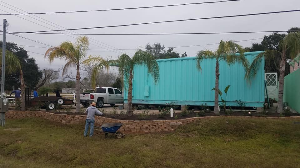 A man is pushing a wheelbarrow in front of a blue building.