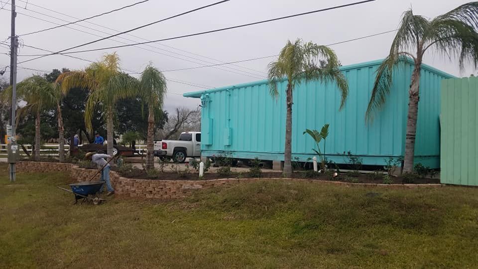 A man is pushing a wheelbarrow in front of a blue house.