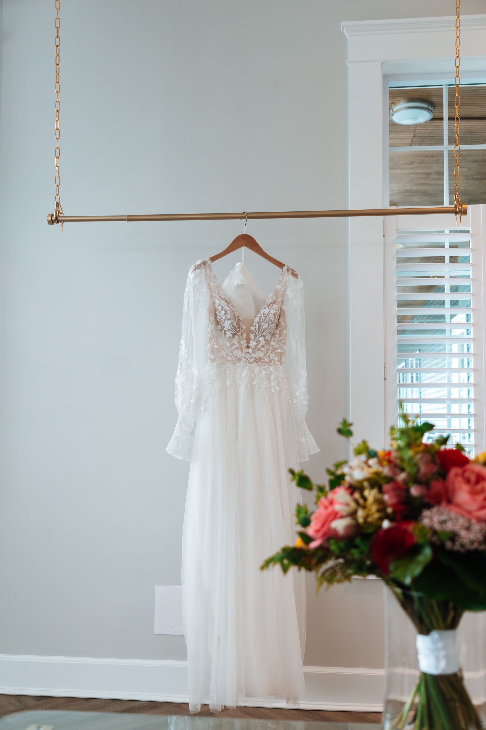 A wedding dress is hanging on a rack next to a vase of flowers.