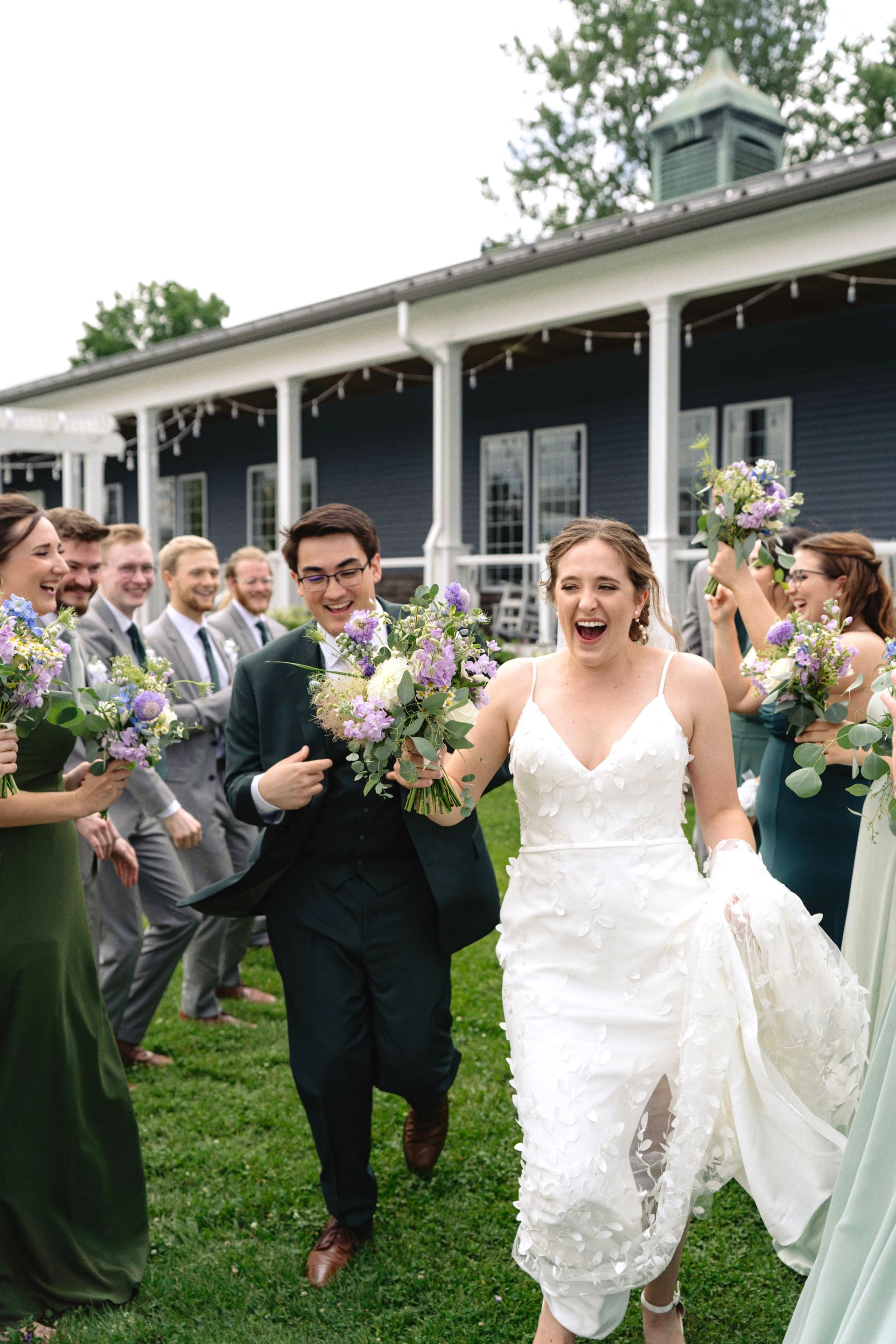 A bride and groom are running with their wedding party in front of a building.