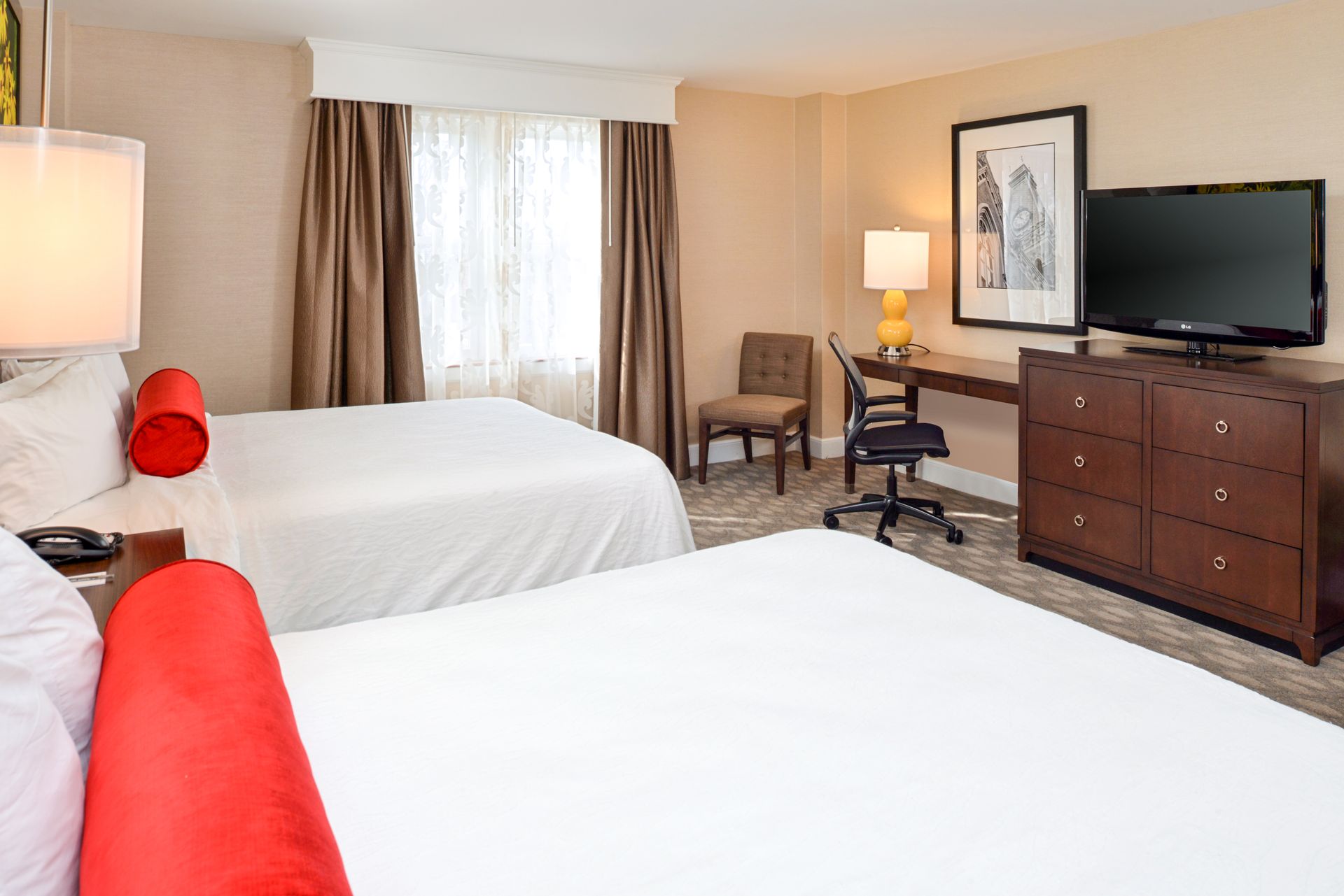 A hotel room with two beds , a desk and a flat screen tv.