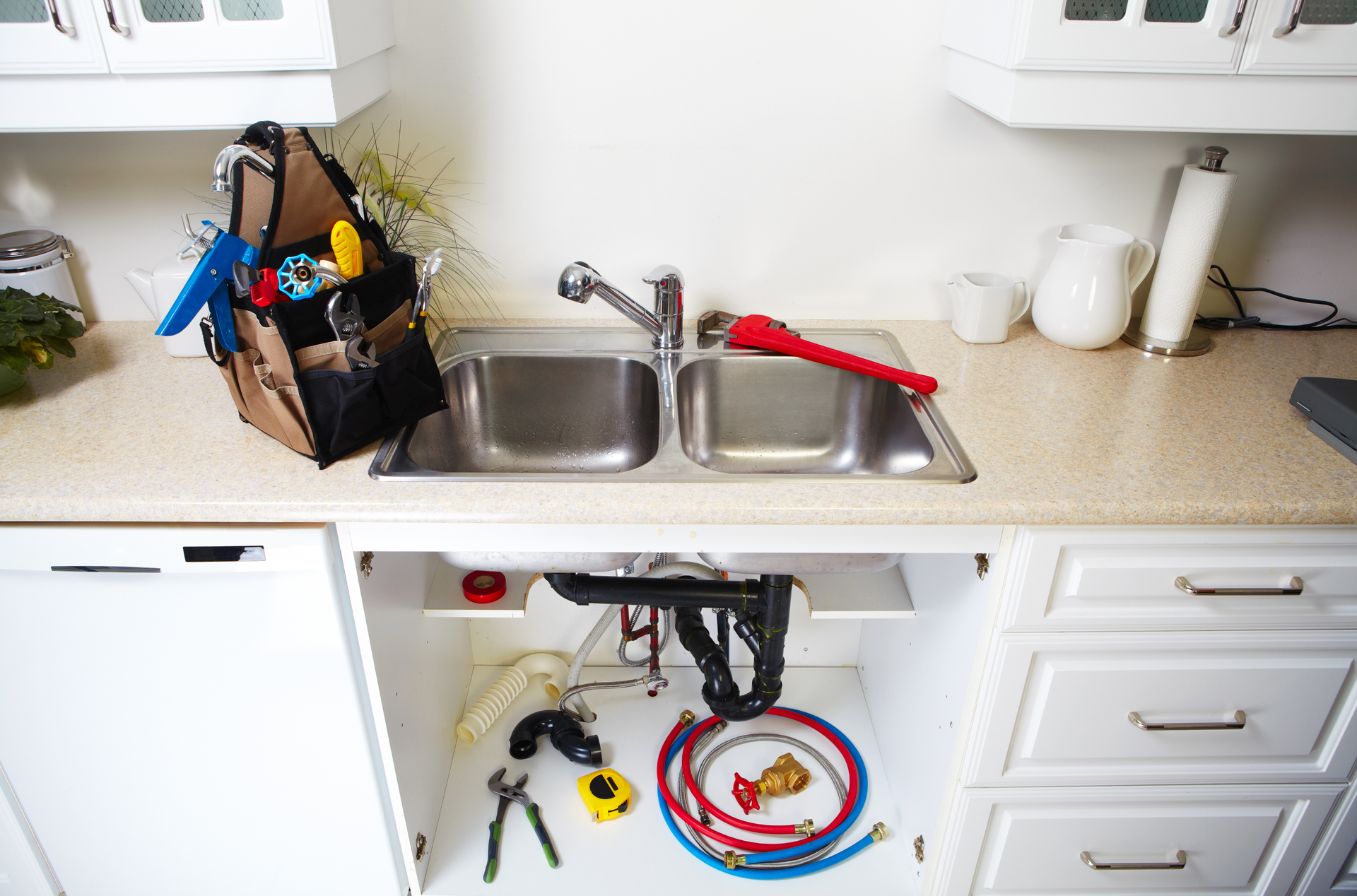 Kitchen sink with open cabinet, plumbing tools, toolbox, and supplies.