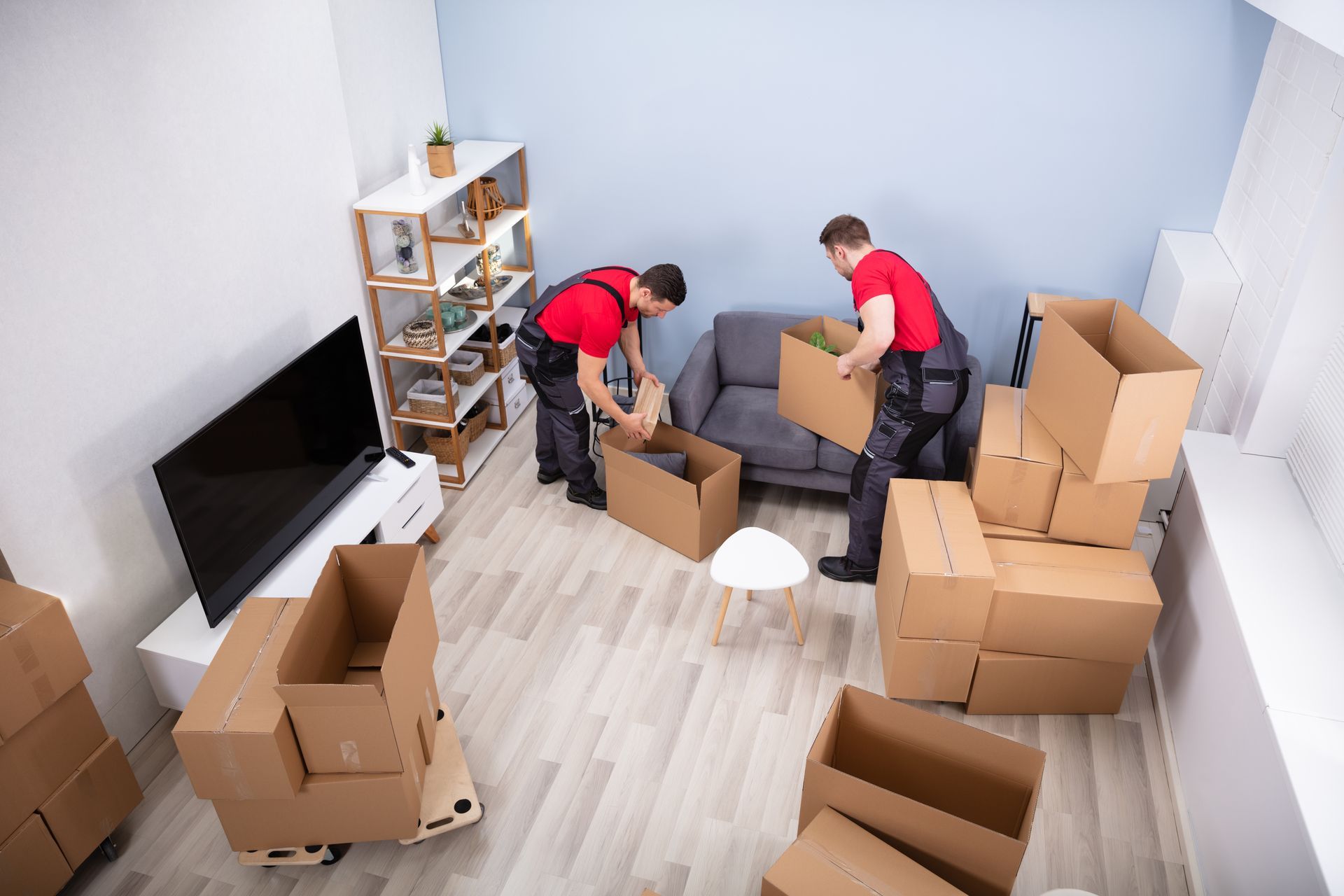 Two Young Movers In Uniform Picking And Putting Products In The Cardboard Boxes

