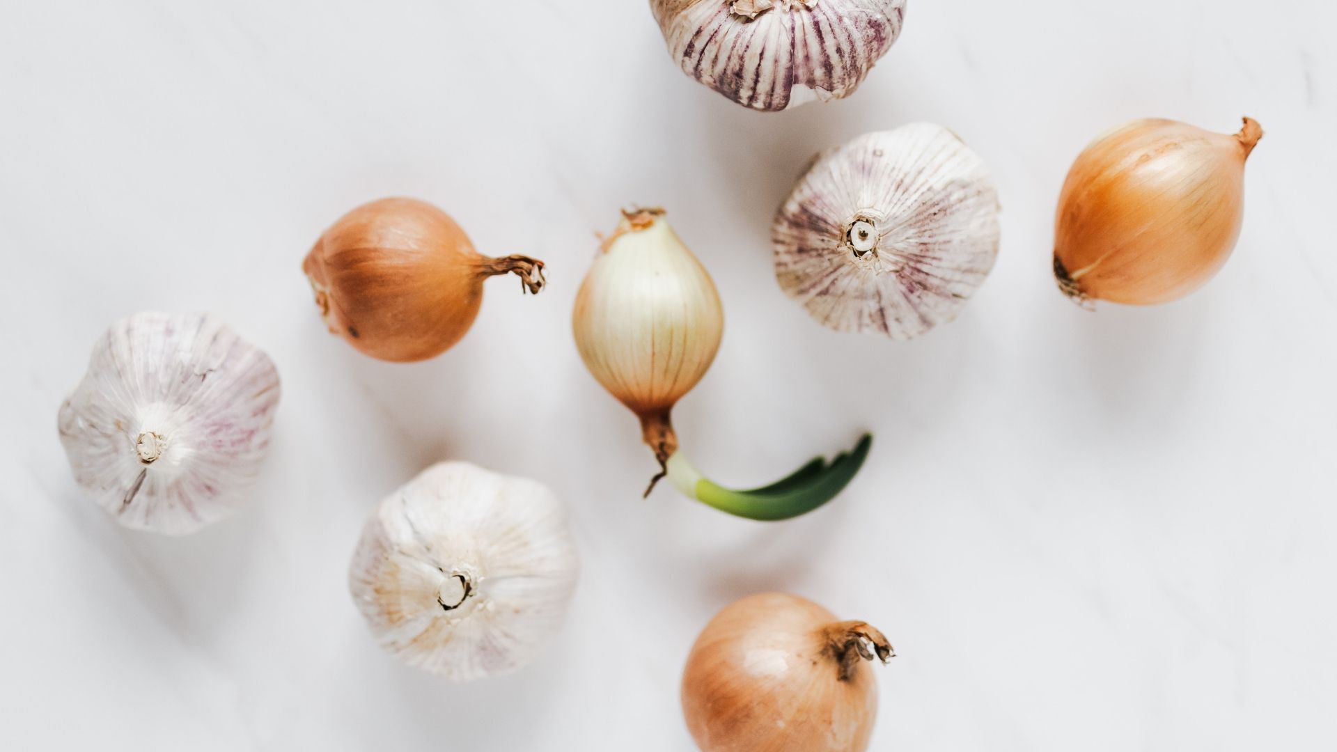 Several bulbs of garlic and small yellow onions scattered on a plain white surface.