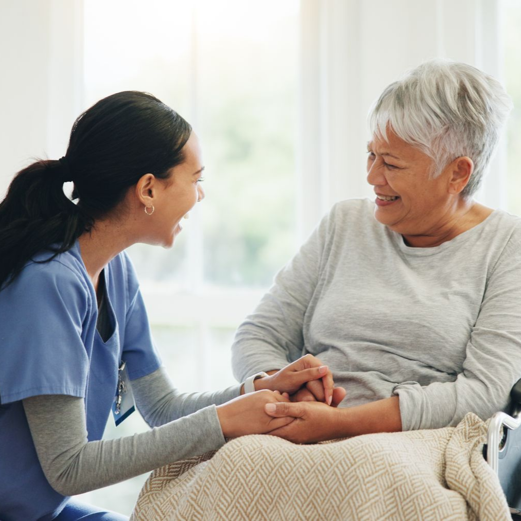 A caregiver, wearing a blue uniform, provides senior care to a senior in a wheelchair. A caregiver, wearing a blue uniform, provides senior care to a senior in a wheelchair.