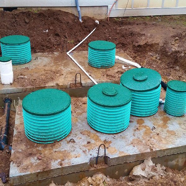 Green septic tank lids on concrete in a muddy construction site.