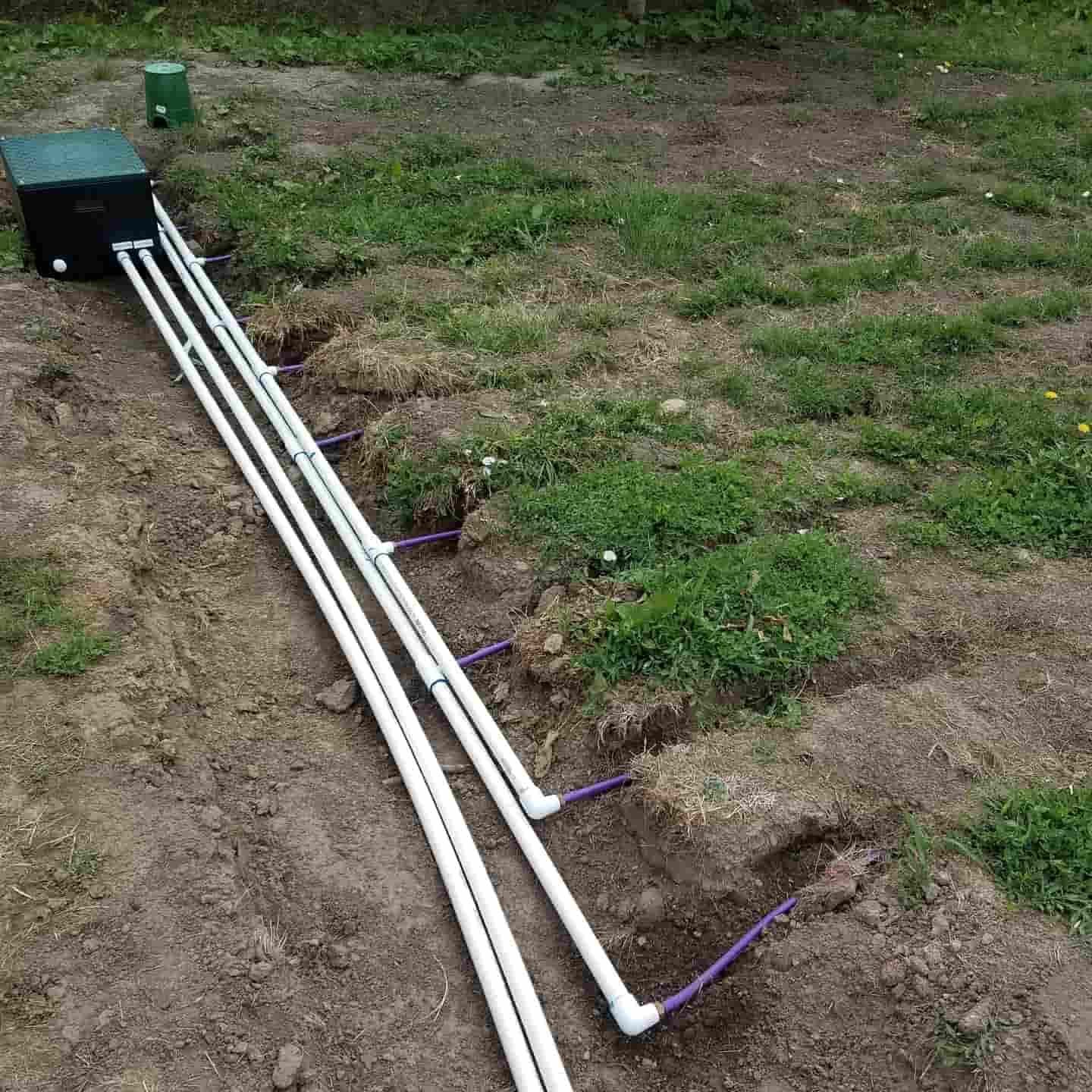 White PVC pipes and a black box connect to soil trenches; septic system installation outdoors.