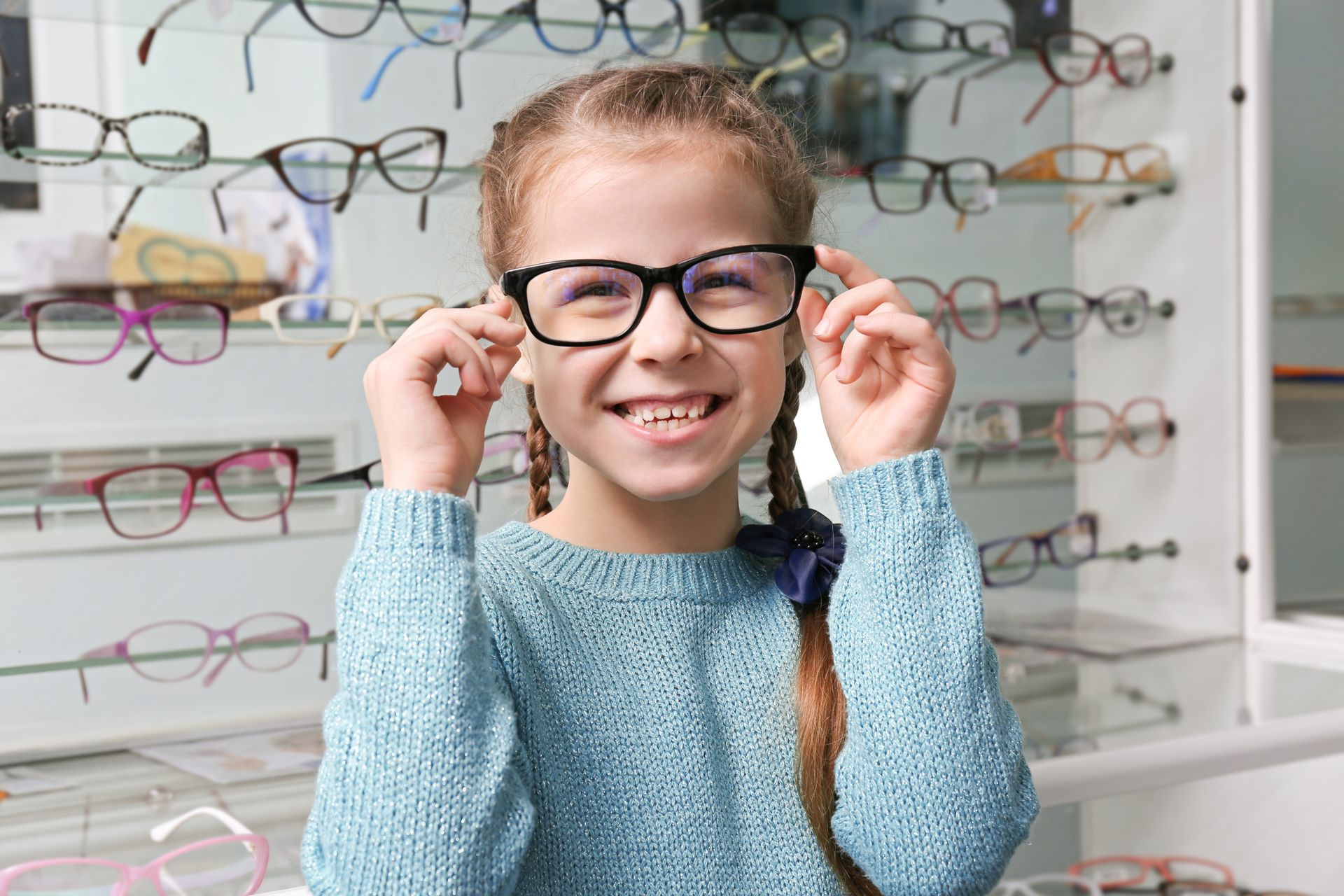 Smiling child adjusting black glasses in an eyeglasses shop