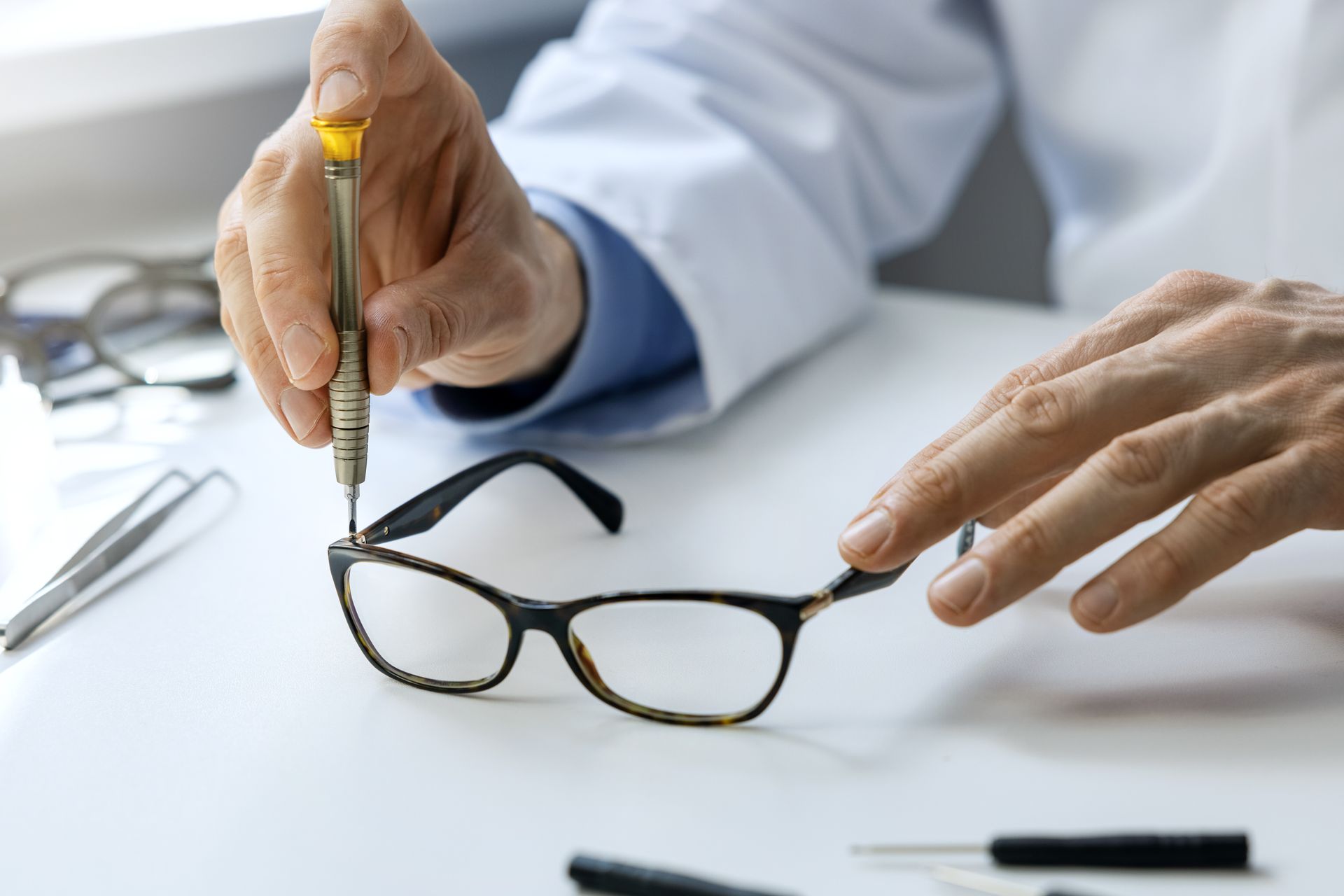 Hands adjusting black eyeglasses with a small screwdriver on a white desk