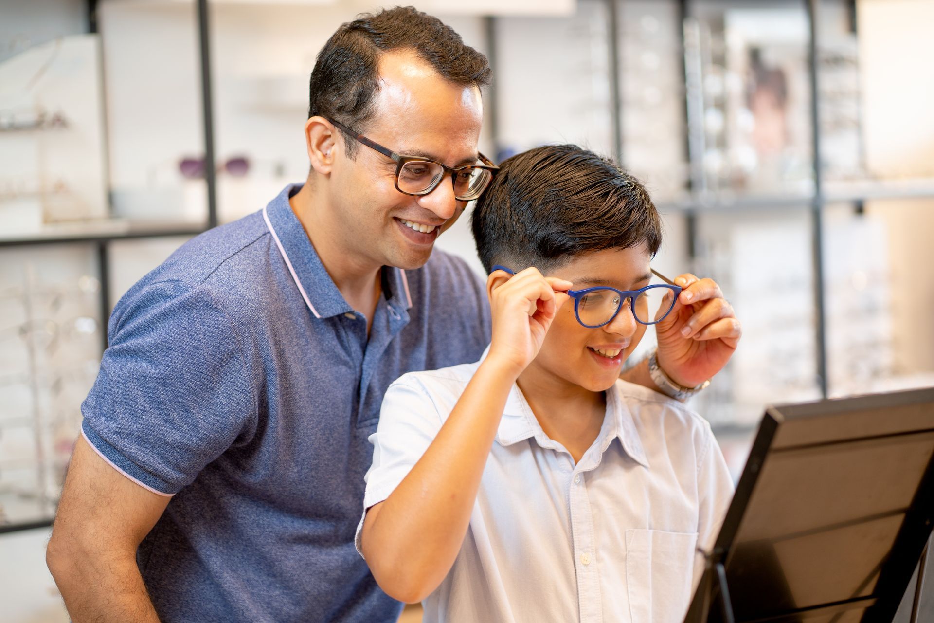 Adult helping a child adjust glasses while looking at a computer in a bright room