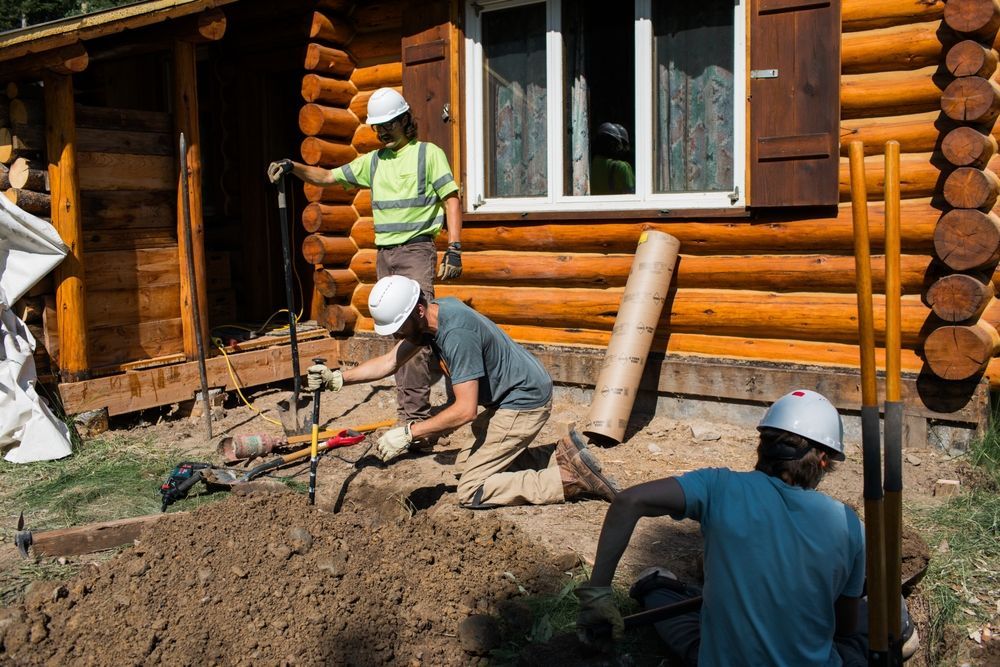 A group of construction workers are working in front of a log cabin.
