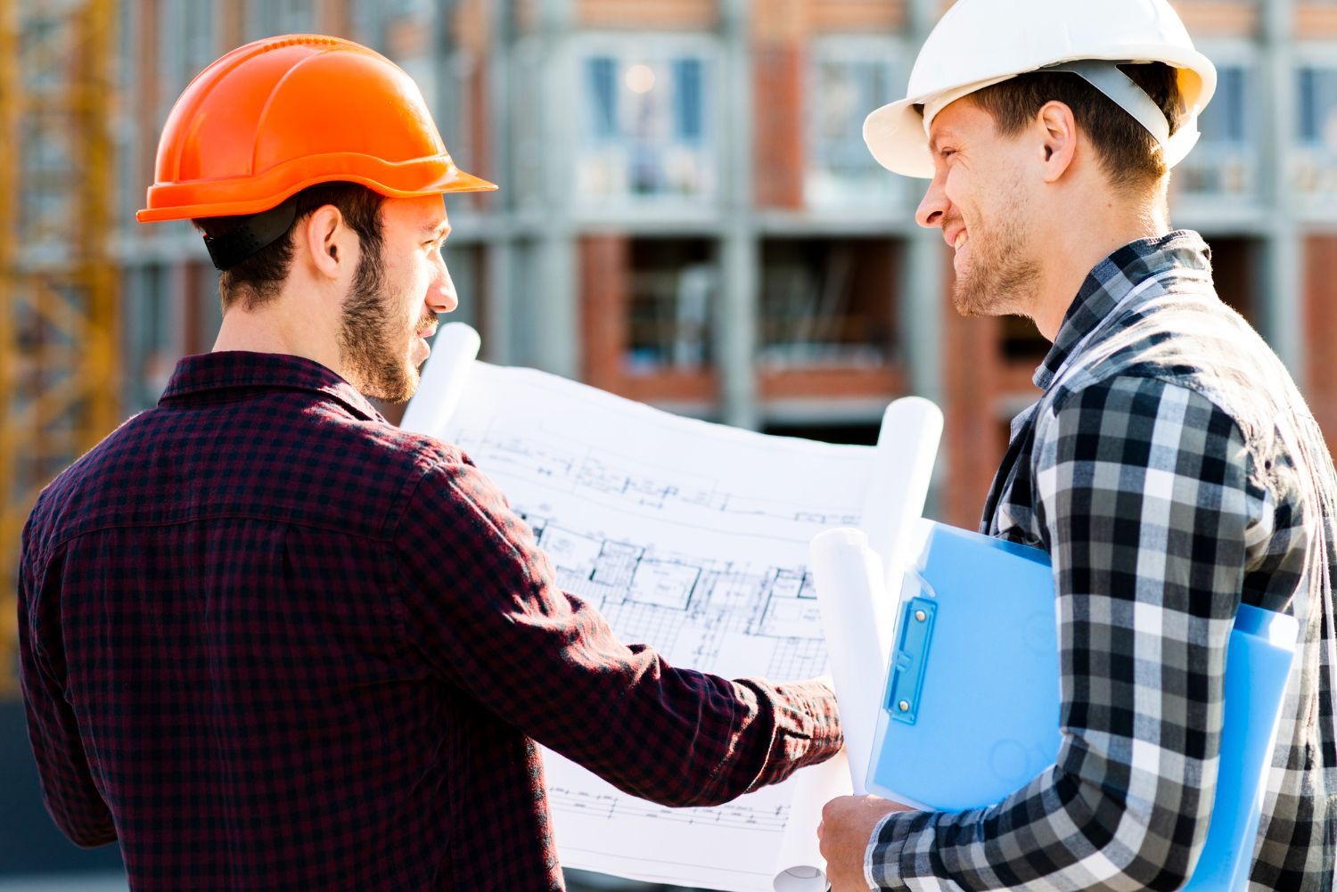 Two construction workers are looking at a blueprint on a construction site.