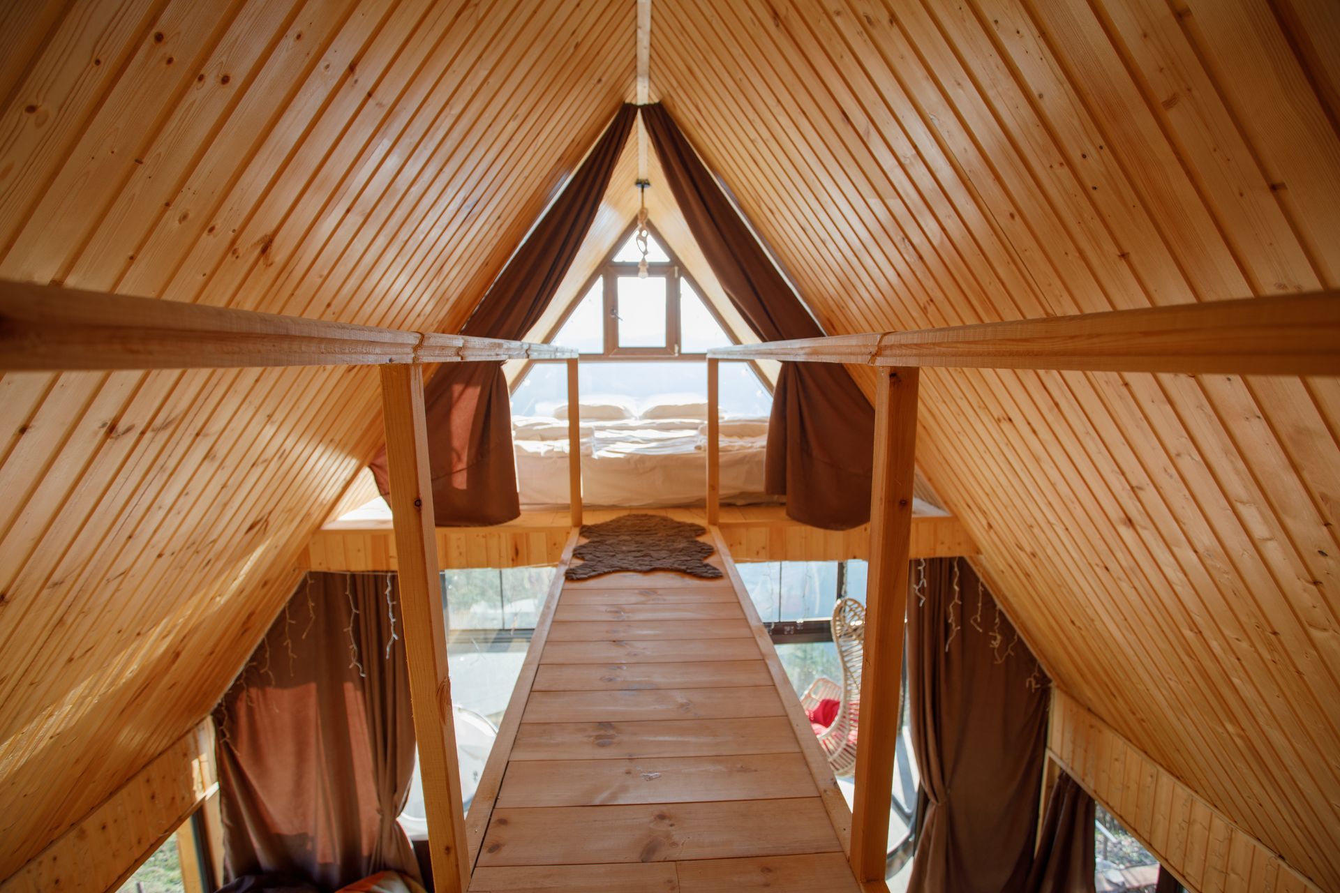 Wooden interior with triangular ceiling and loft overlooking a view. Brown curtains frame the opening.