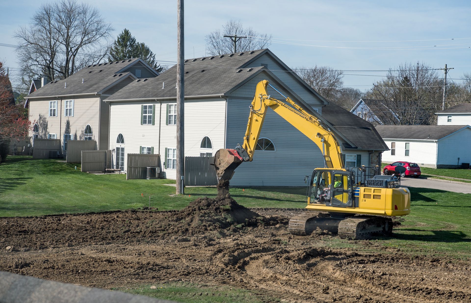 Yellow excavator digging dirt beside a suburban house on a grassy lot