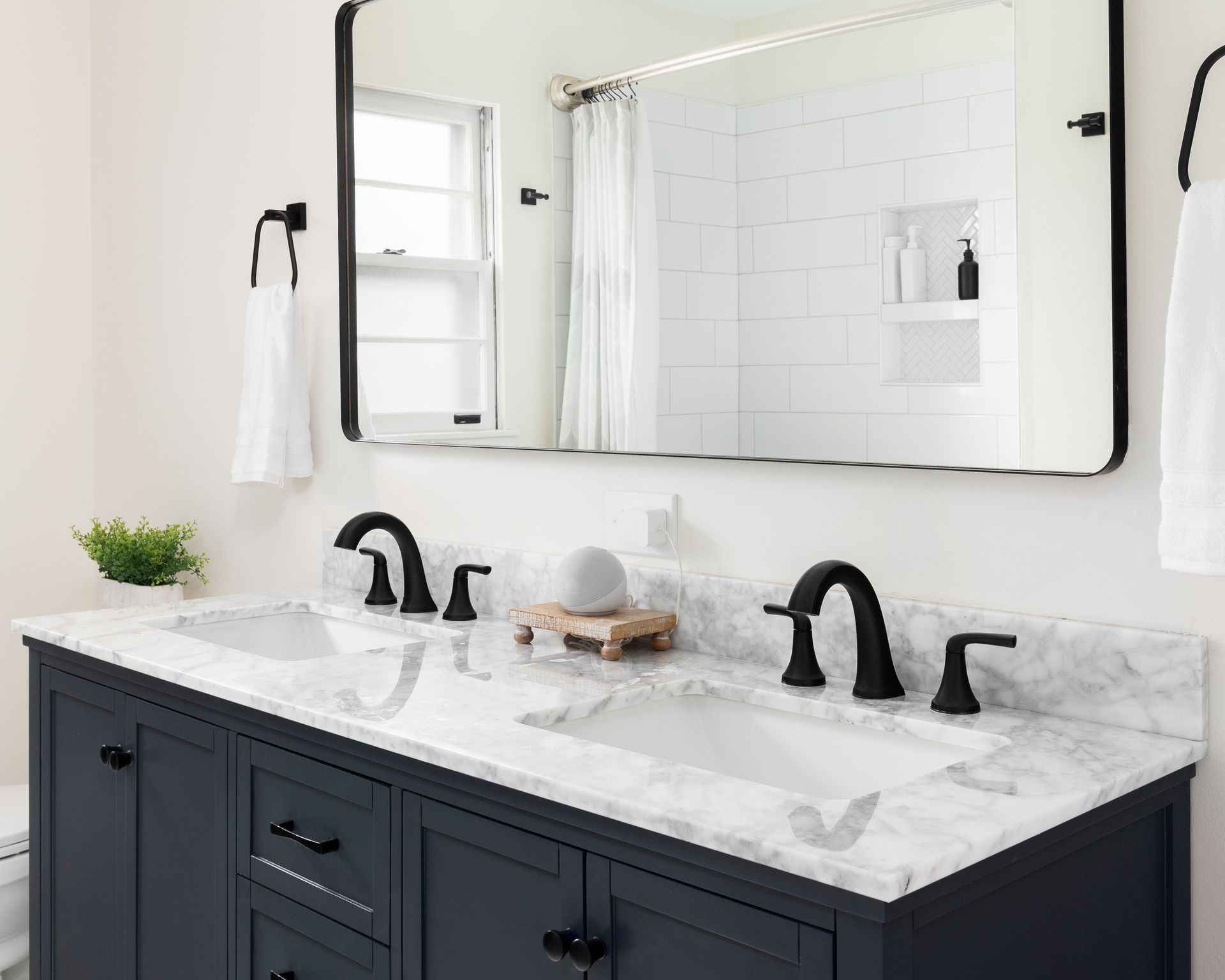 Bathroom with navy vanity, marble countertop, black fixtures, and large mirror.