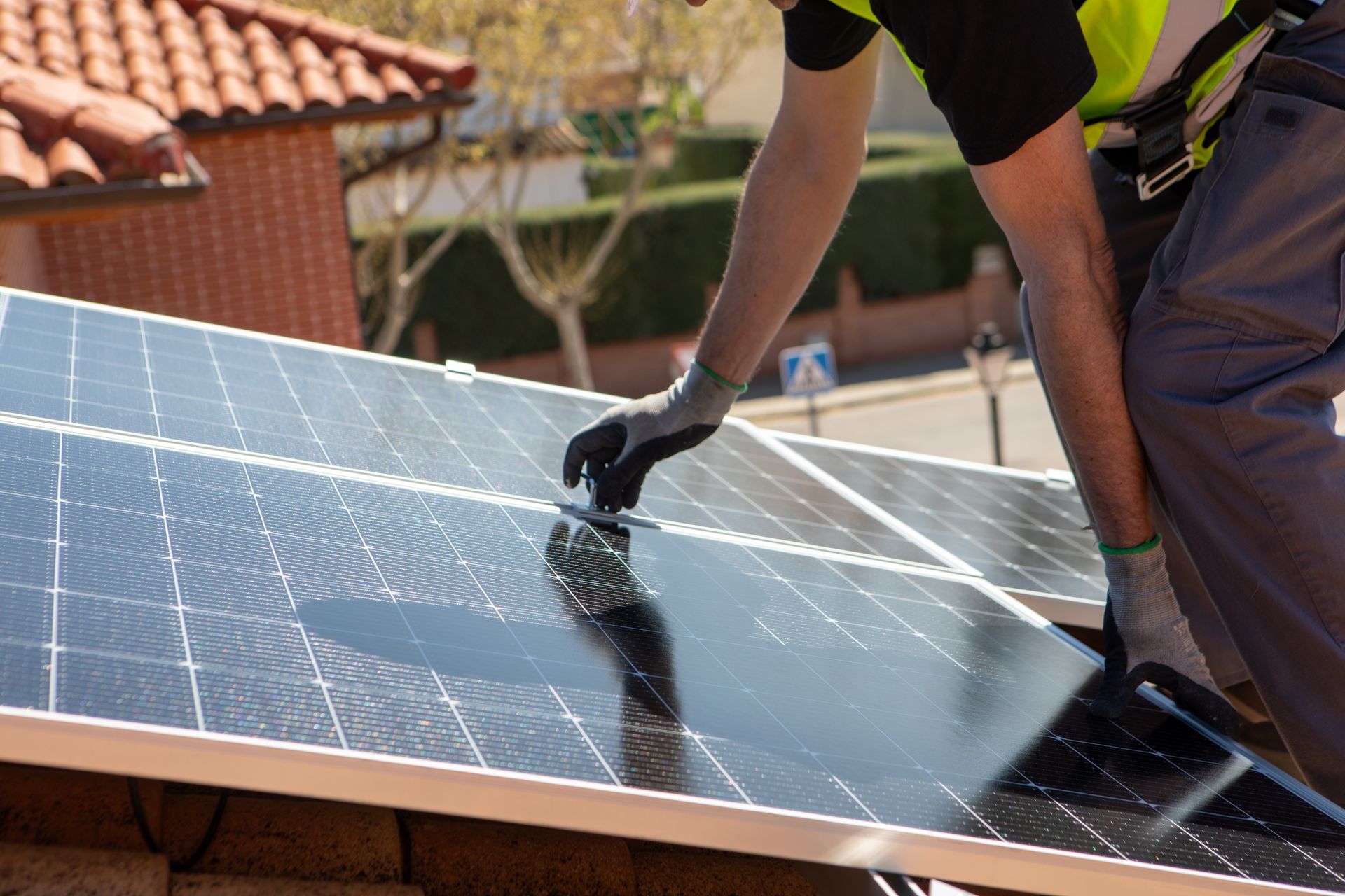 Worker installing solar panels on a rooftop, wearing gloves and safety vest.