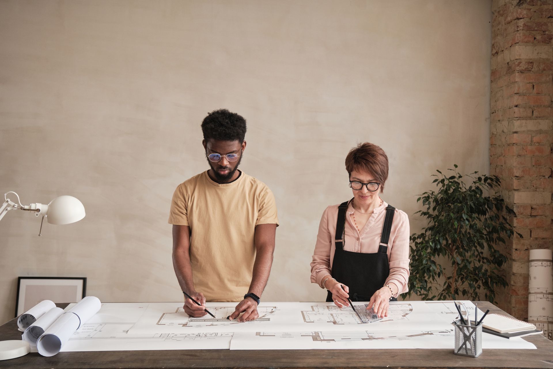 A man and a woman are standing at a table looking at a blueprint.