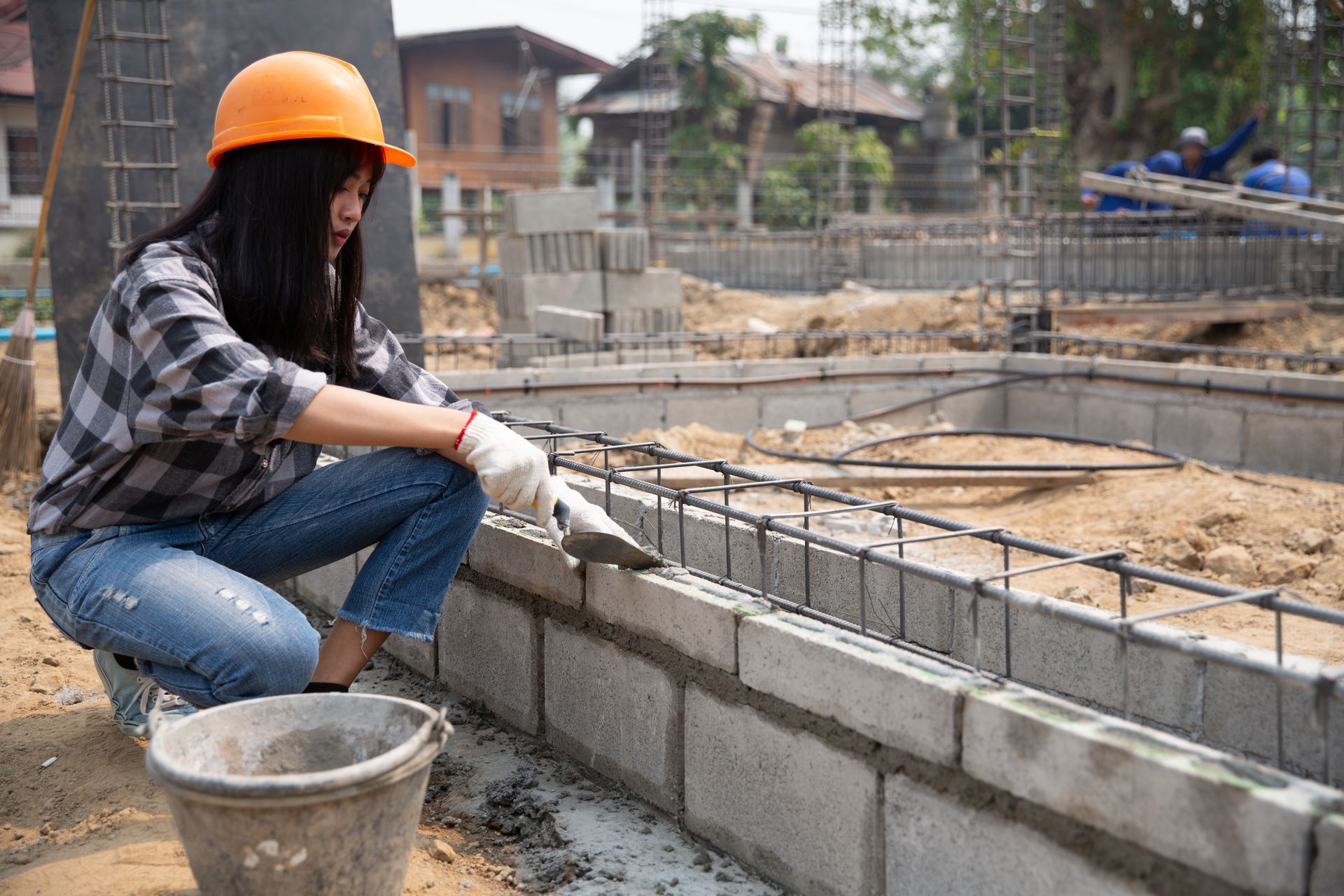 A woman is working on a brick wall at a construction site.