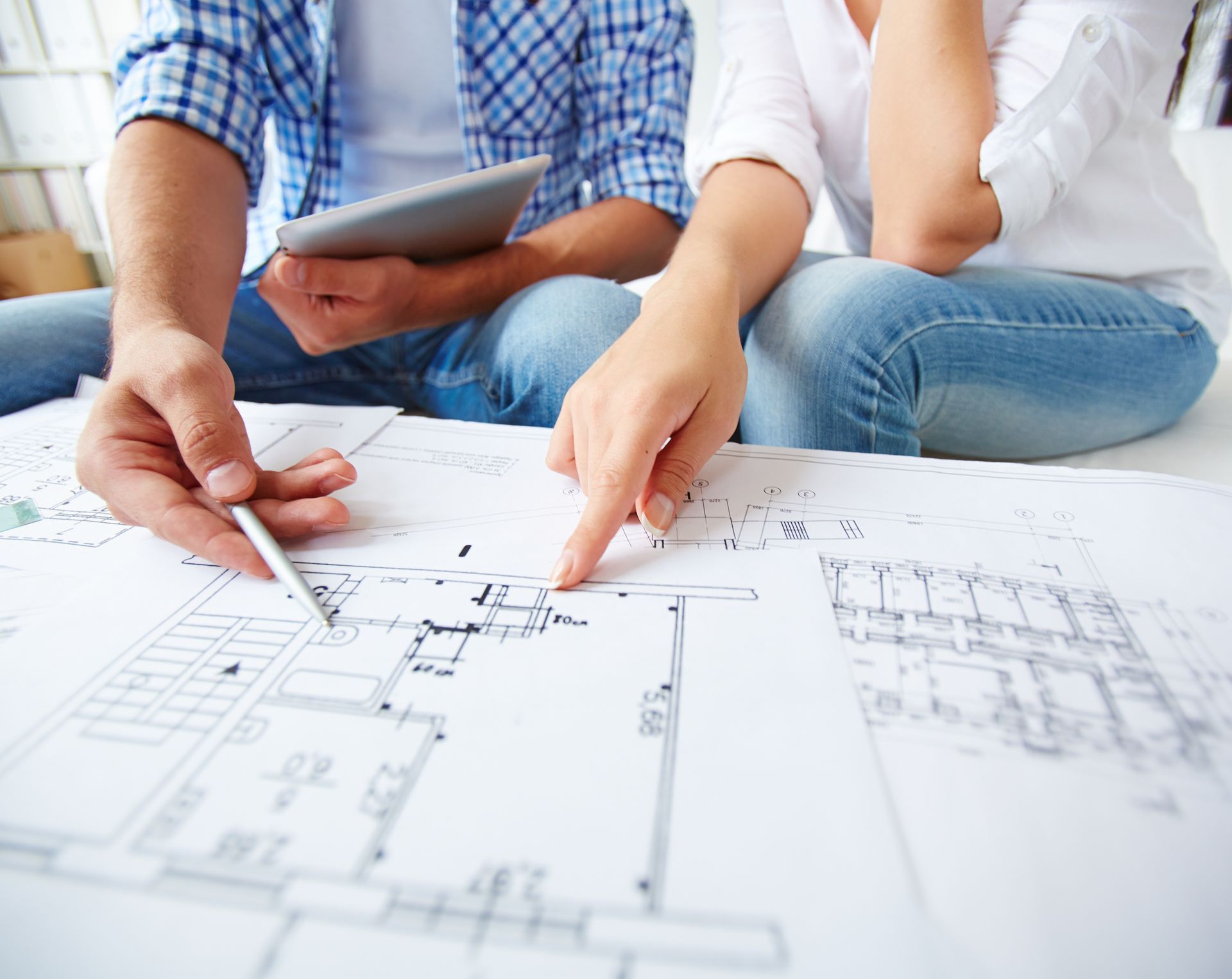 A man and a woman are sitting on the floor looking at a floor plan.