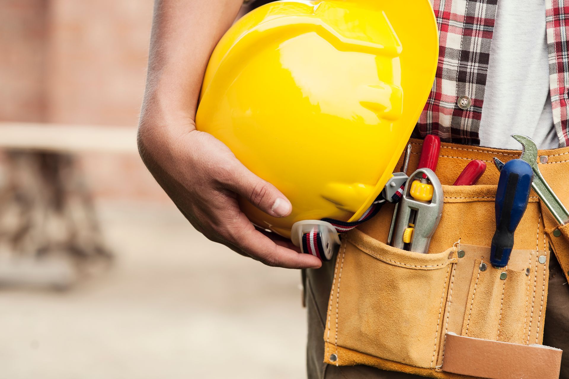 A construction worker is holding a hard hat and a tool belt.