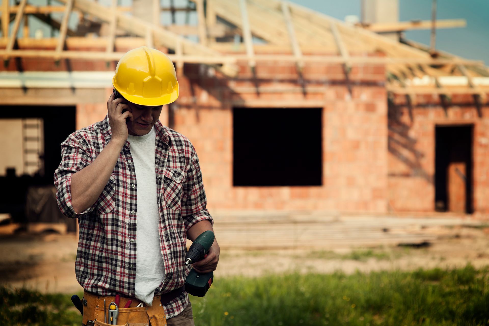 A construction worker is talking on a cell phone in front of a building under construction.
