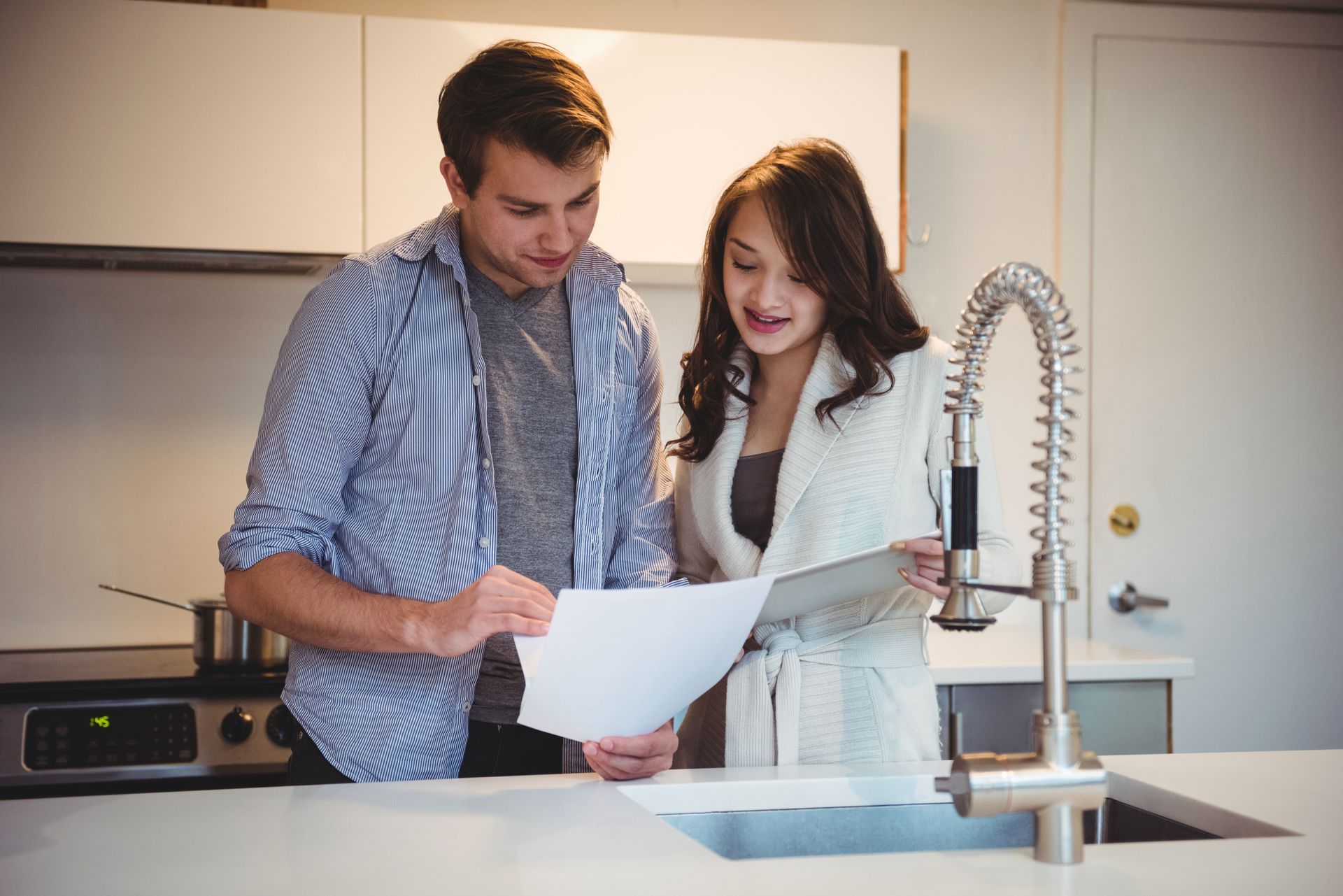 A man and a woman are looking at a piece of paper in a kitchen.