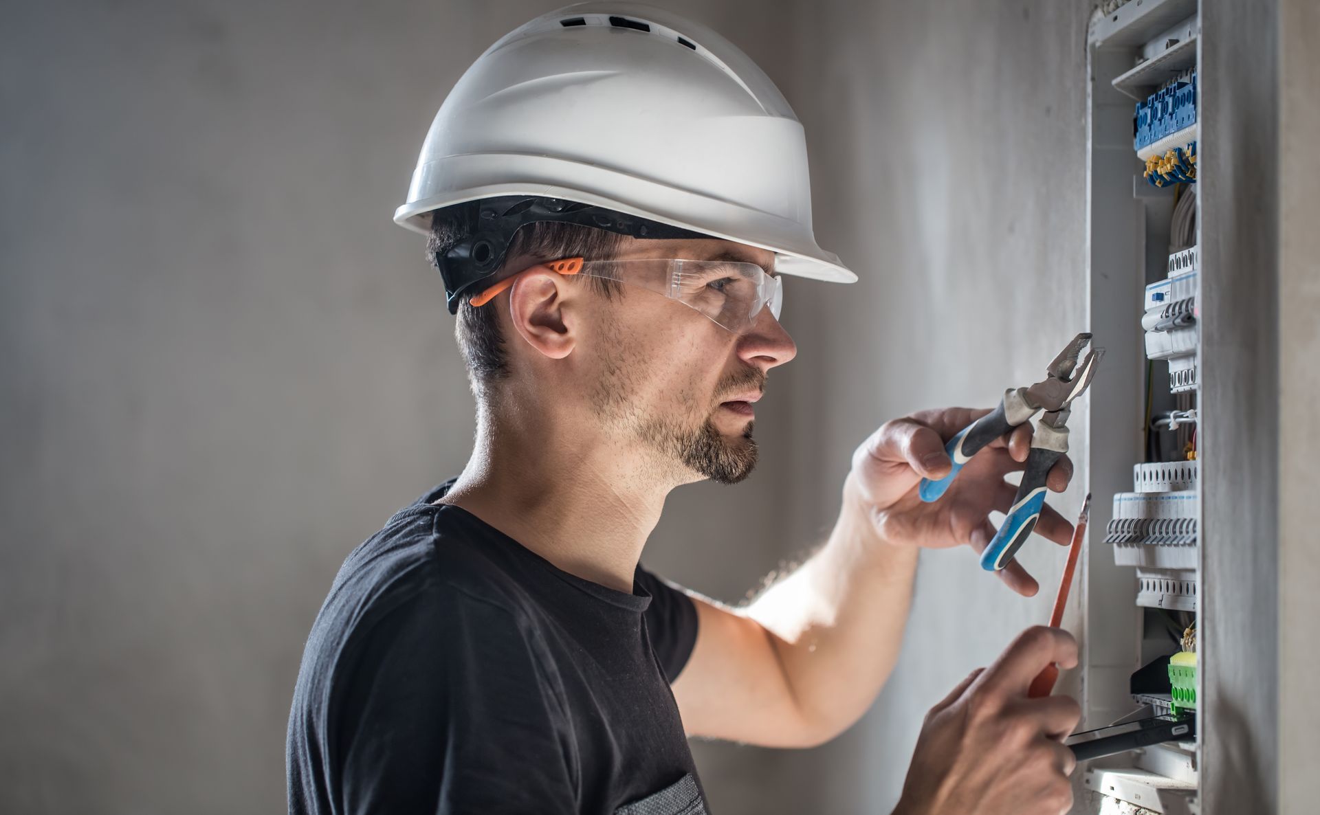 A man wearing a hard hat and safety glasses is working on an electrical box.