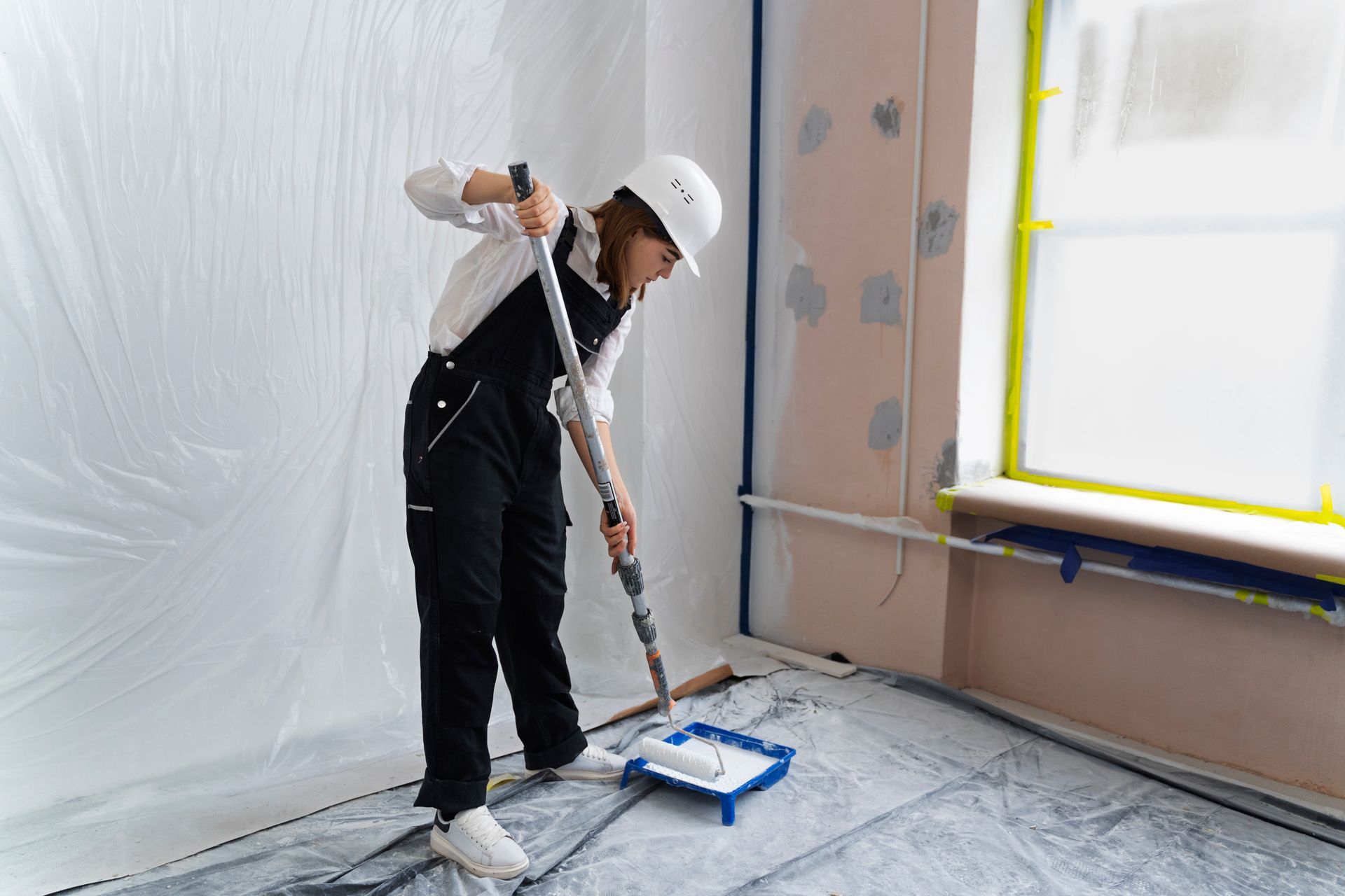 A woman is dipping the roller to get fresh painting on the wall