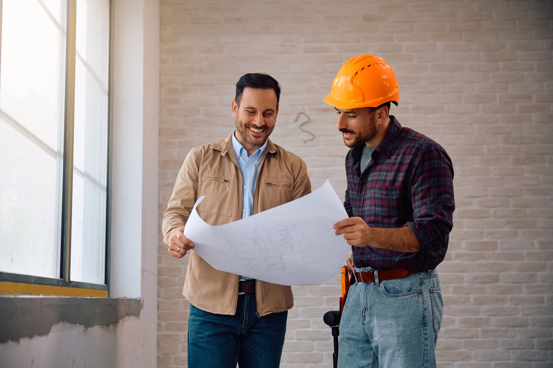 Two construction workers are looking at a blueprint in a room.