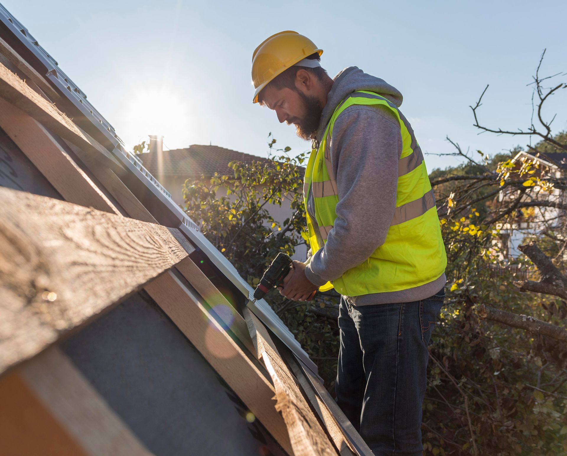 A man wearing a hard hat and safety vest is working on a roof.