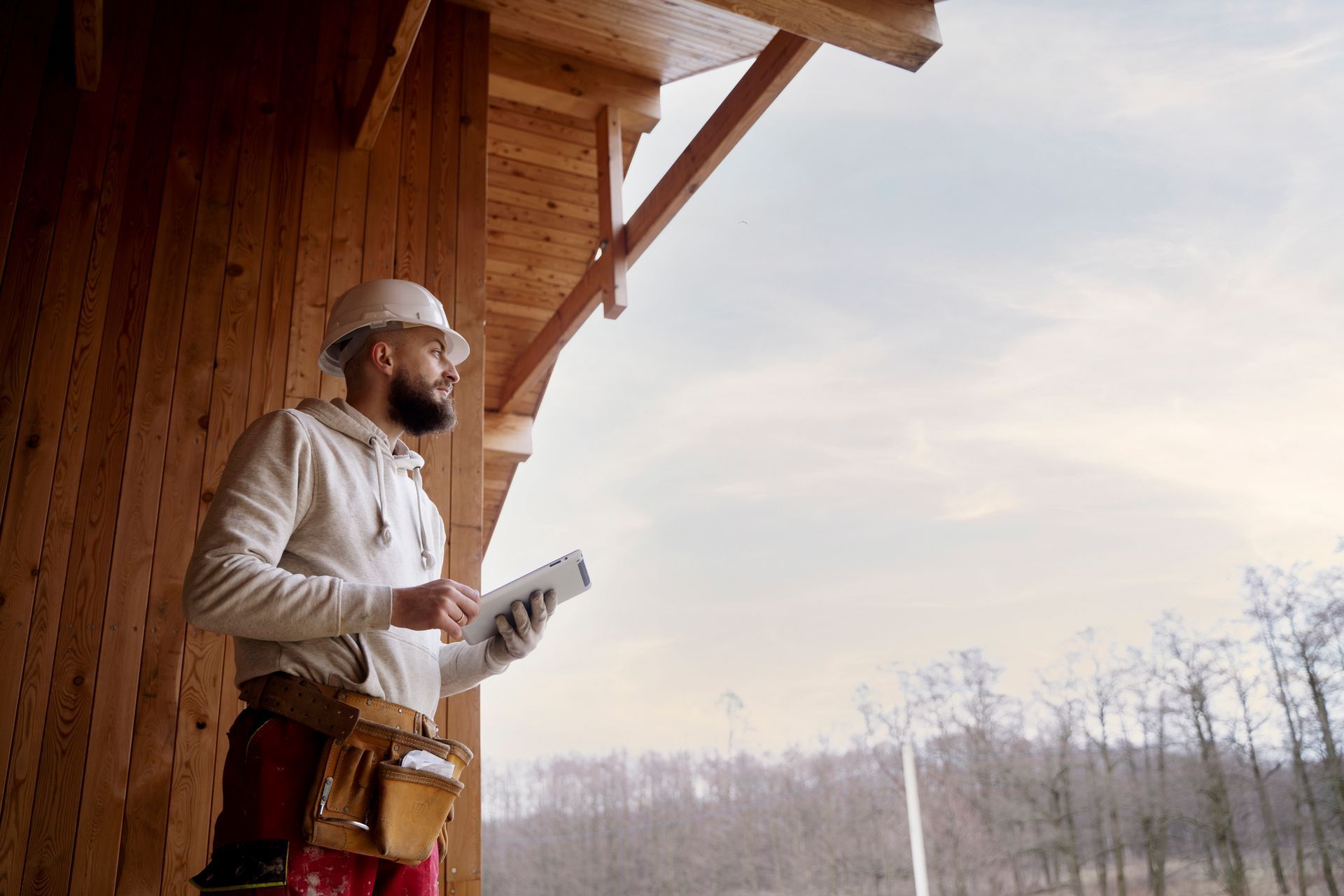 A construction worker is looking out of a window while holding a tablet.